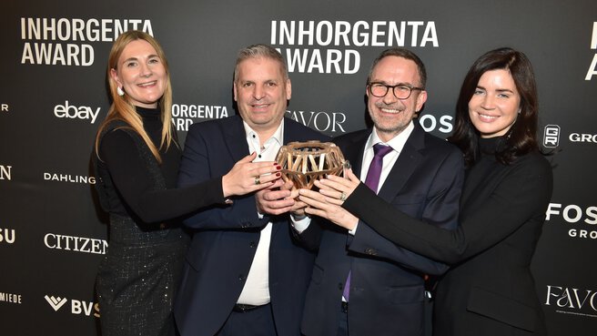 Four people smile and hold the trophy for the “Fine Jewelry of the Year” category in front of a logo wall at the INHORGENTA AWARD Gala.