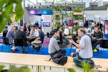 Menschen sitzen und diskutieren in einem modernen Konferenzbereich mit blauem Boden und Grünpflanzen und tauchen ein in die Welt der Quantentechnologie.