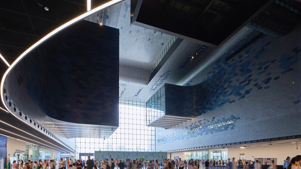 The interior of a hall-like futuristic building with curved light strips on the ceiling and numerous visitors.