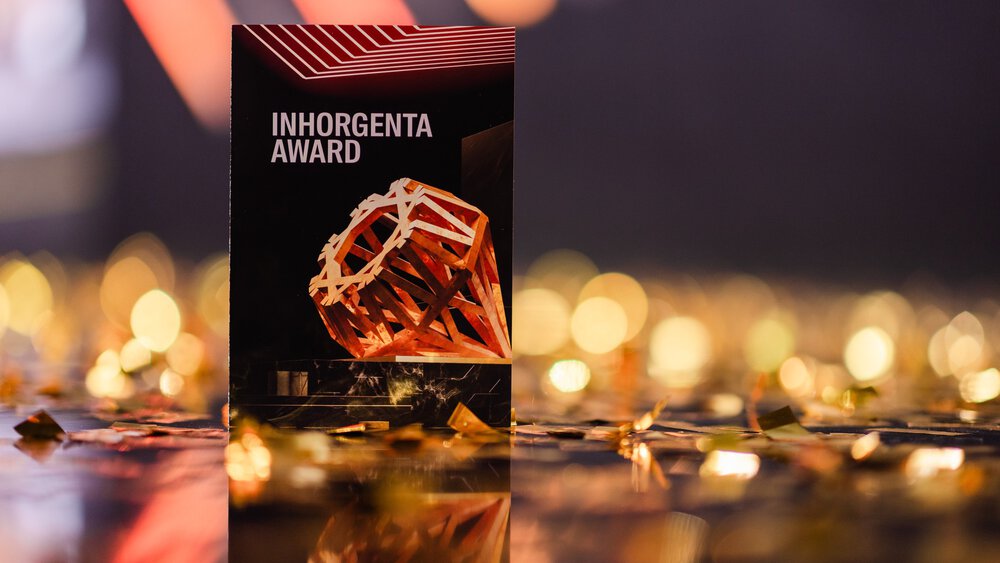 Ein Schild mit der Aufschrift INHORGENTA AWARD mit einer geometrischen Skulptur, umgeben von goldenem Konfetti.