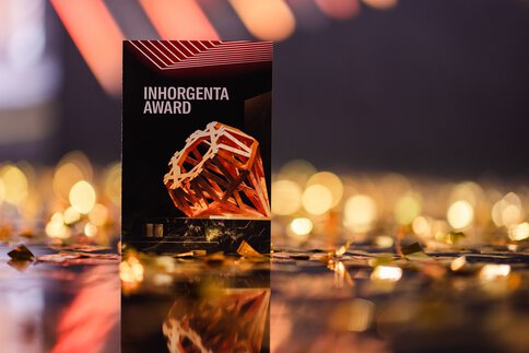 A sign bearing the inscription INHORGENTA AWARD with a geometric sculpture surrounded by golden confetti.