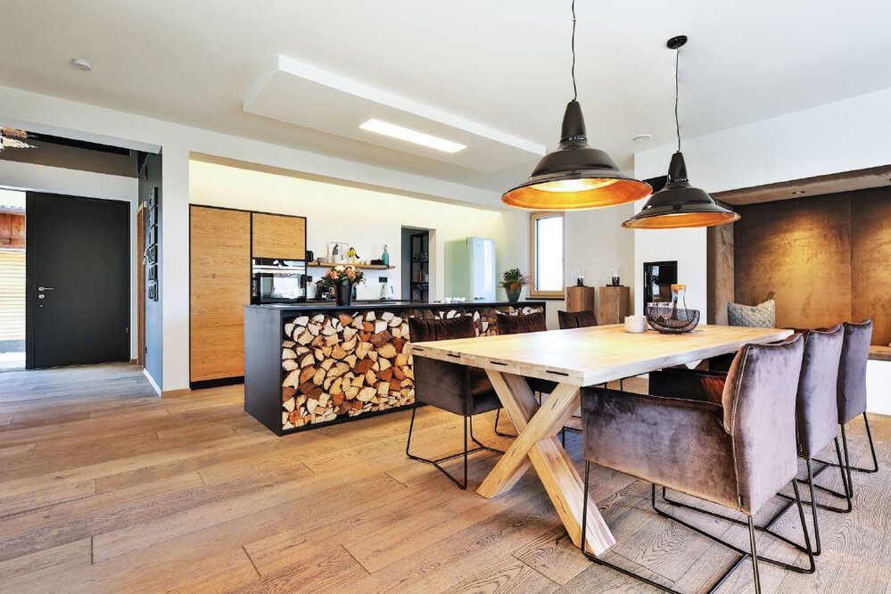 Moderne Küche und Essbereich mit Holzböden, großem Tisch, Hängelampen und eleganten Geräten.