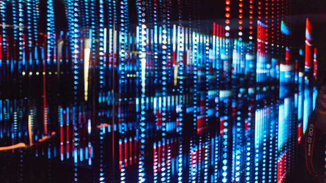 Lichtinstallation mit vielen kleinen, wie Perlenschnüre aufgehängen roten und blauen Lichtern die einen effektvollen Gesamteindruck ergeben.