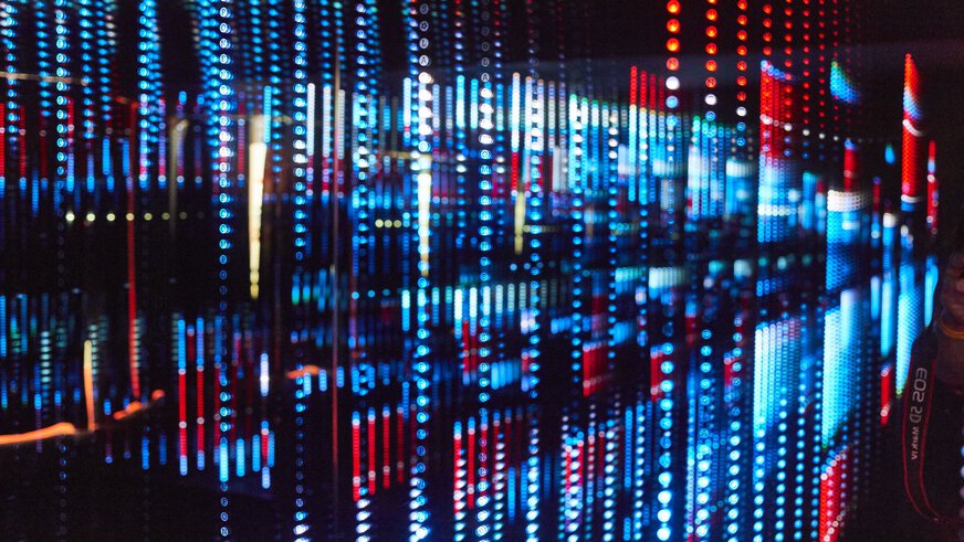 Lichtinstallation mit vielen kleinen, wie Perlenschnüre aufgehängen roten und blauen Lichtern die einen effektvollen Gesamteindruck ergeben.