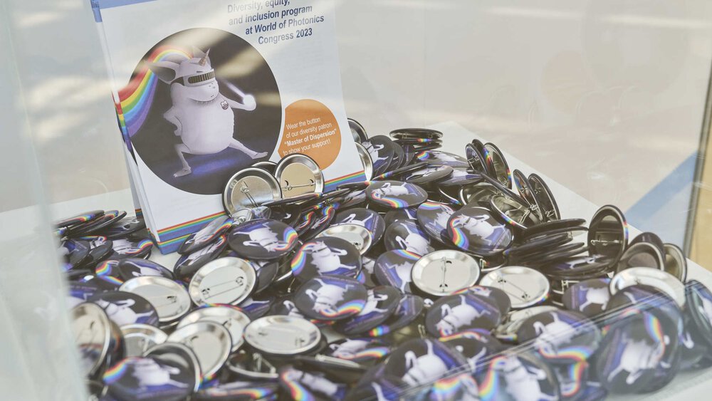 A box full of pins with a cartoon unicorn and flyers with texts promoting diversity, equality and inclusion.