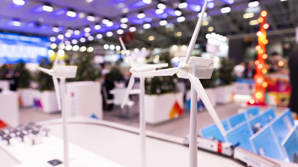 Drei weiße Modellwindräder stehen auf einer Präsentationsfläche der electronica. Ein Modellzug fährt auf Schienen um den Aufbau herum.