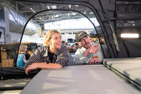 Zwei Personen betrachten ein Dachzelt im Ausstellungsbereich Caravaning & Camping auf der f.re.e. Das Bild zeigt modernes Camping mit Dachzelt und passt zur Podcast-Folge über Dachzelte und Outdoor-Abenteuer.