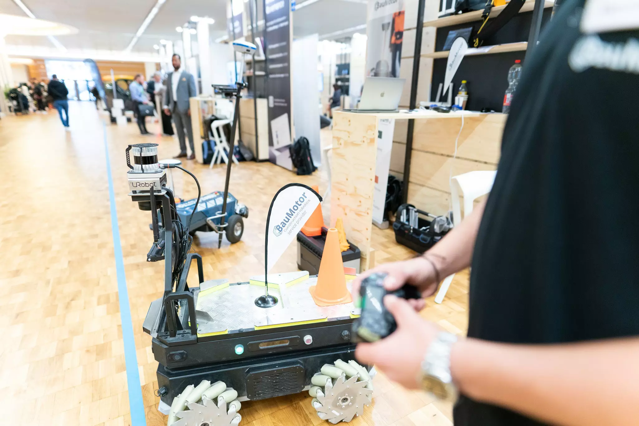 Mitarbeiter von BauMotor mit Handy steuert einen fahrenden Roboter in der Startup Area der bauma 2022