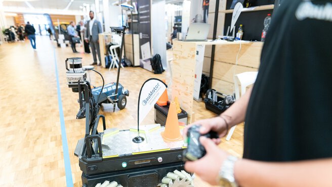 BauMotor employee with cell phone controls a moving robot in the Startup Area at bauma 2022