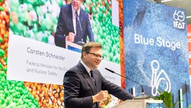Carsten Schneider speaking at the lectern in front of a screen displaying his name and title as Federal Minister.