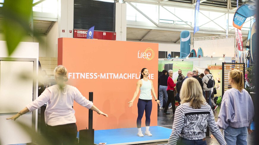 Trainer leads a fitness session in the hands-on area at the “f.re.e” trade fair, while visitors actively participate.