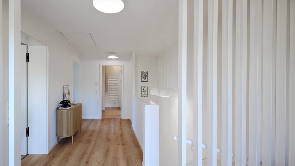 Heller Flur mit Holzboden, weißen Wänden und vertikalen weißen Lamellen neben einem Treppenabgang.