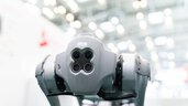 Roboterhund mit vier Kameras in einer hellen, industriellen Umgebung, nach vorne gerichtet.