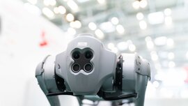 Robot dog with four cameras in a bright, industrial environment, facing forward.