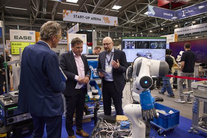 Drei Männer im Gespräch an einem Robotik-Stand in der Start-up-Arena.