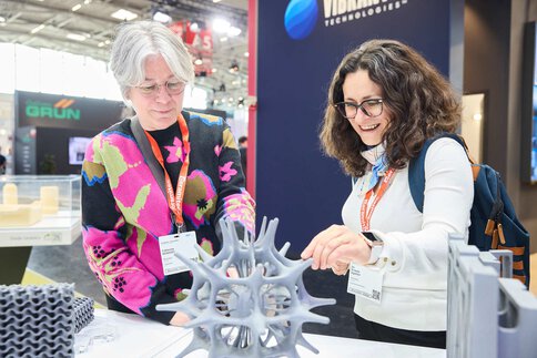 Two trade fair visitors examine a complex ceramic exhibit together at a booth.