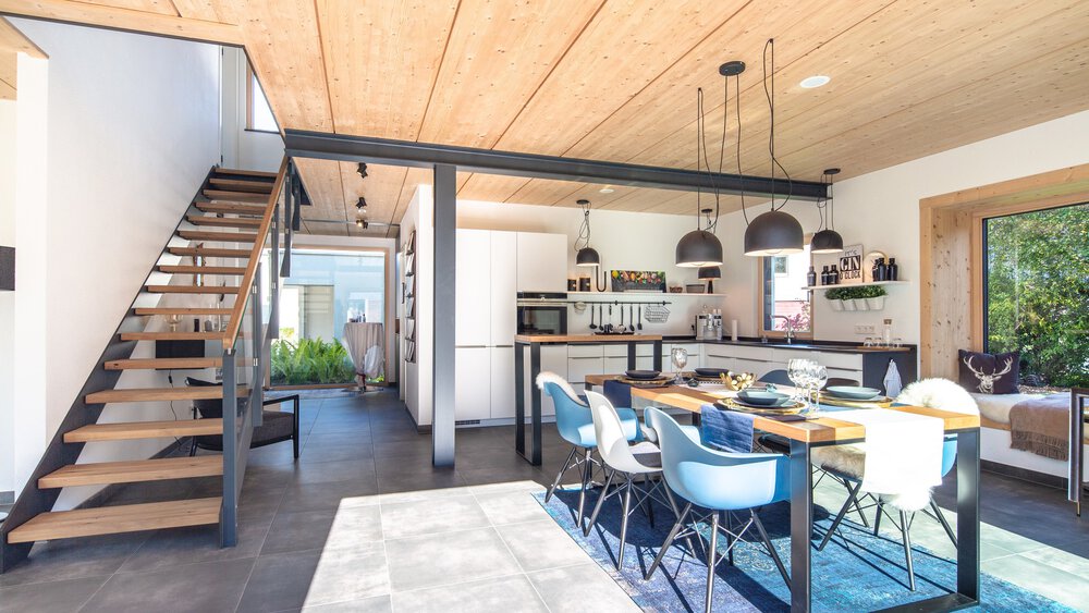 Offener Küchen- und Essbereich mit Holzdecke, Treppe und moderner Einrichtung. Der Raum ist von natürlichem Licht durchflutet.