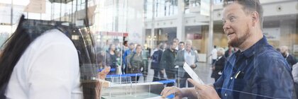 Ein Mann spricht mit einer Frau an einem Ticketschalter in der Eingangshalle der Messe.