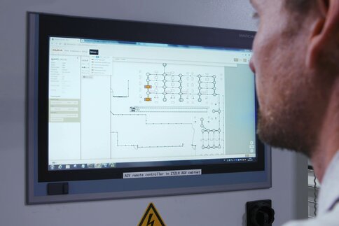 Schulterblick bei einem Mann mit kurzem Bart, der einem großen Bildschirm ein Interface zur Fernsteuerung betrachtet.