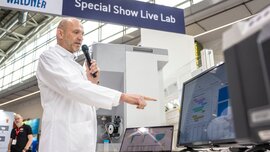 A scientist in a white lab coat presents analysis results on a screen at the “Special Show Live Lab” at analytica.