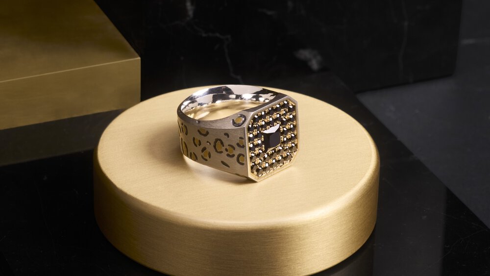 A silver and gold ring with black gemstones on a round gold platform against a dark background.