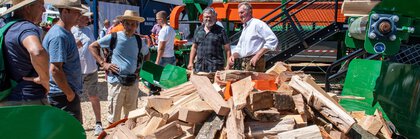 Männer betrachten Holzspaltmaschine mit Brennholz auf einer Vorführung im Freigelände einer Fachmesse.