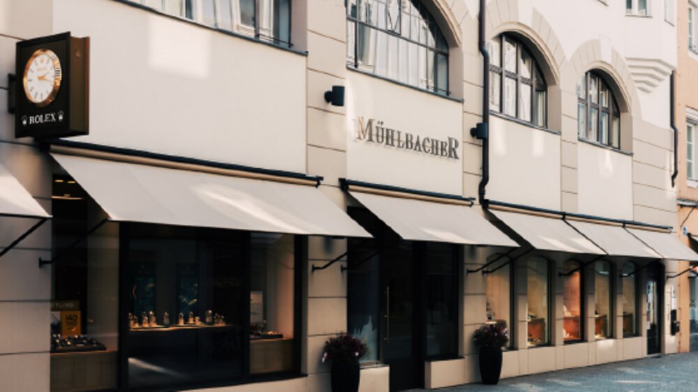 The exterior facade of a jewelry store called Mühlbacher in beige with extended awnings for the shop windows.