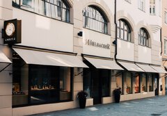 The exterior facade of a jewelry store called Mühlbacher in beige with extended awnings for the shop windows.