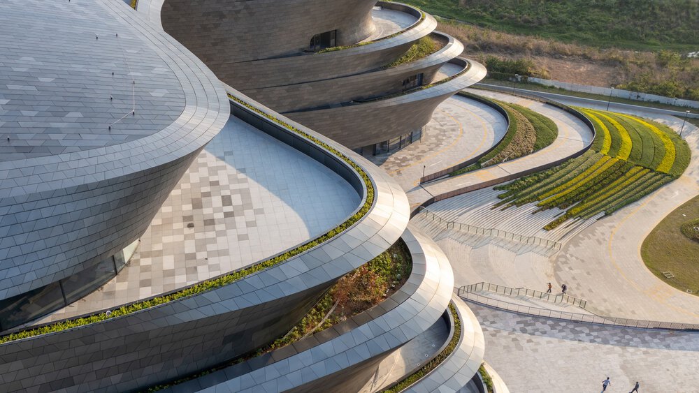 A futuristic building consisting of several levels with curved balconies of varying sizes, which are covered with vegetation at the edges and on individual roofs.