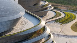 A futuristic building consisting of several levels with curved balconies of varying sizes, which are covered with vegetation at the edges and on individual roofs.