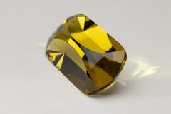 Close-up view of a gemstone with a yellowish color that has been cut multiple times and polished evenly, resting on a white background.