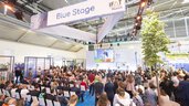Participants in a presentation on the Blue Stage during IFAT Munich in a large exhibition hall.