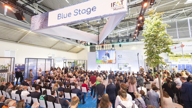 Participants in a presentation on the Blue Stage during IFAT Munich in a large exhibition hall.